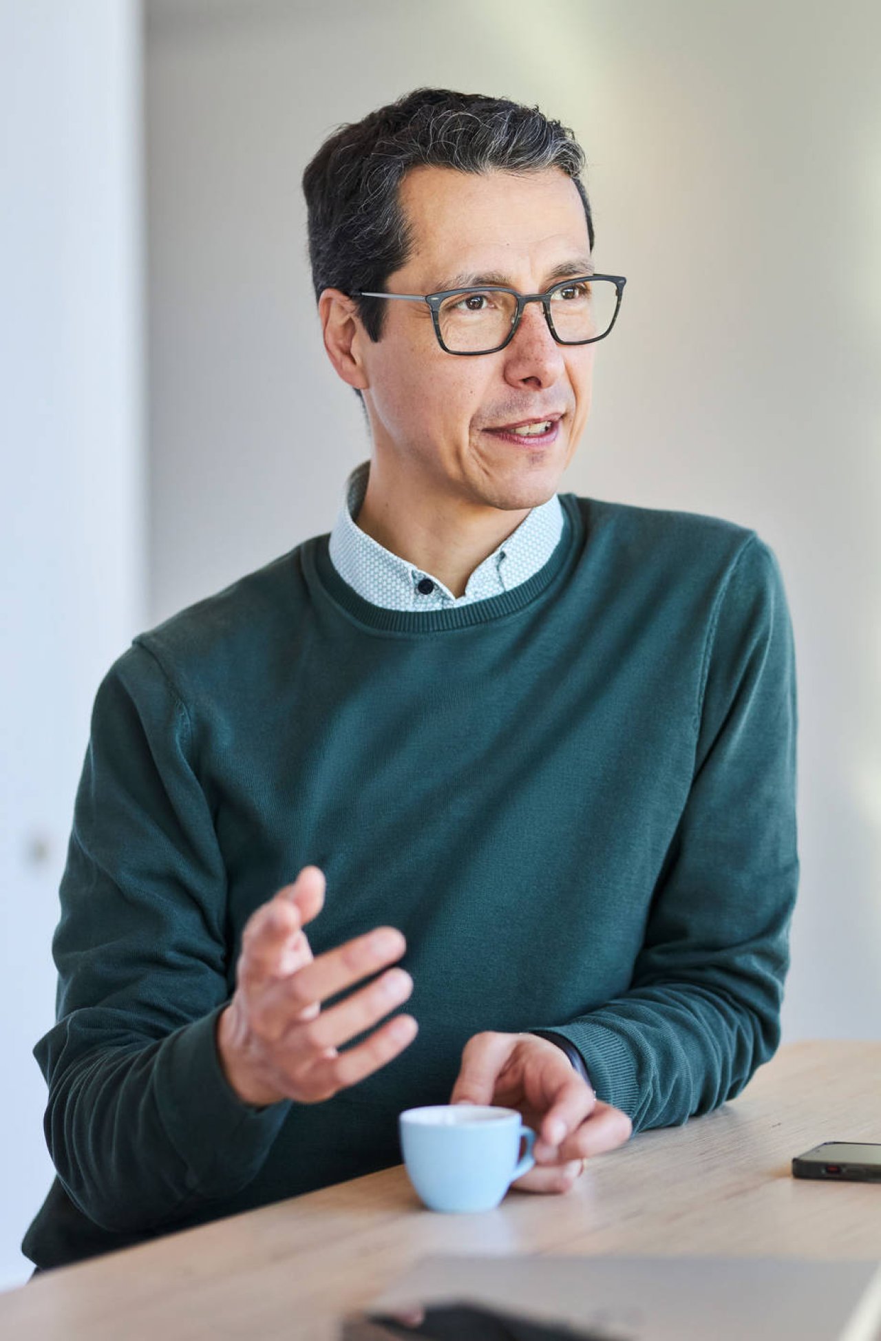 Mittelalter Mann mit dunklen Haaren und Brille steht an einem Tisch und gestikuliert.