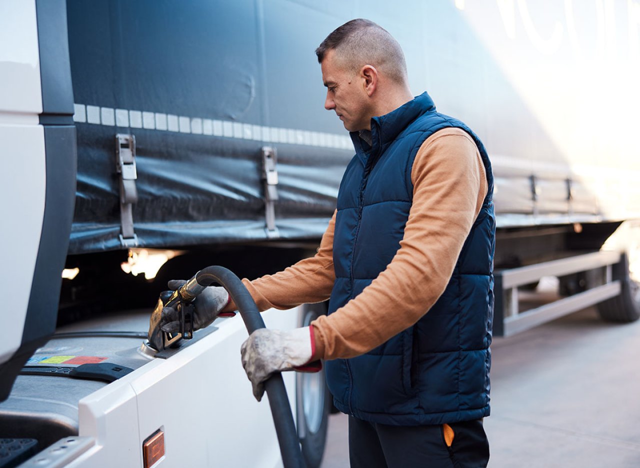 Ein Mann in einer blauen Weste betankt einen LKW.