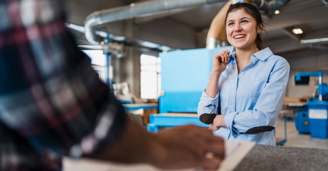 Frau steht in einer Produktionshalle und lächelt.
