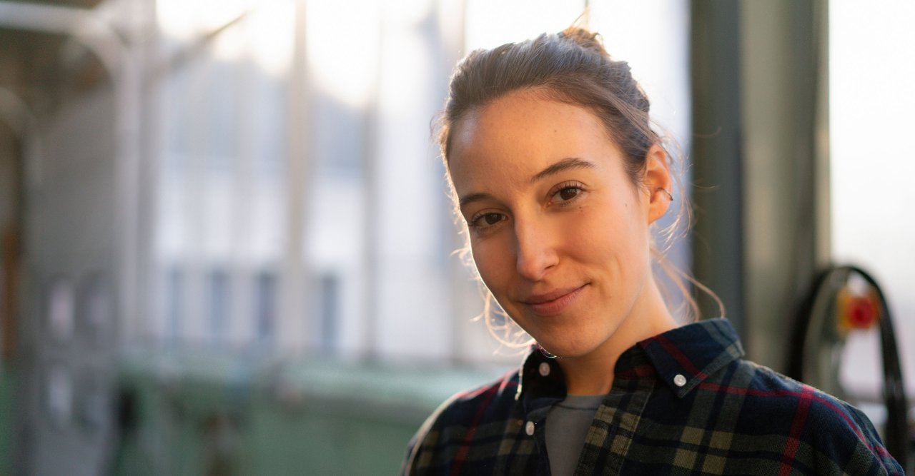 EIne dunkelhaarige Frau mit Karohemd blickt in die Kamera.