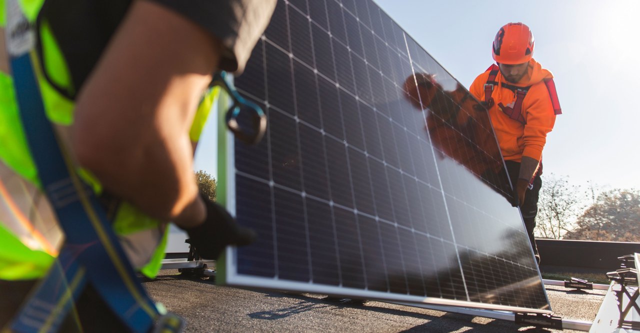 Zwei Männer montieren ein Solarpanel auf einem Dach.