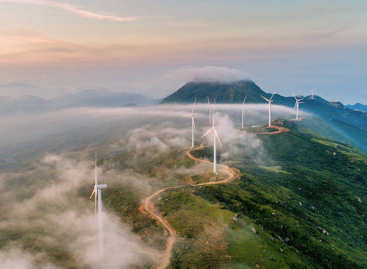 Vogelperspektive auf Windräder und einen Berg im Hintergrund.