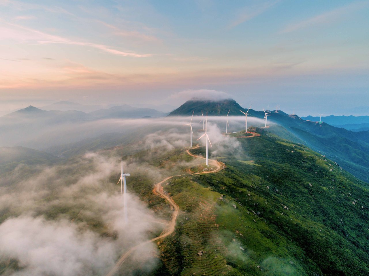Bild aus der Vogelperspektive mit Windrädern, Wiesen und einem Berg.