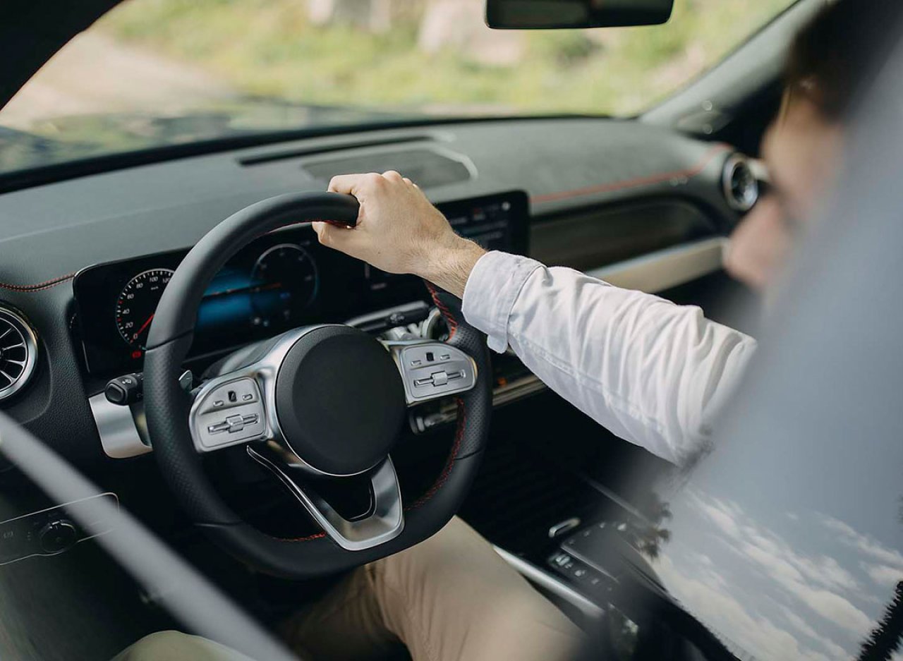 Ein Mann fährt ein Auto und hält das Lenkrad mit einer Hand.