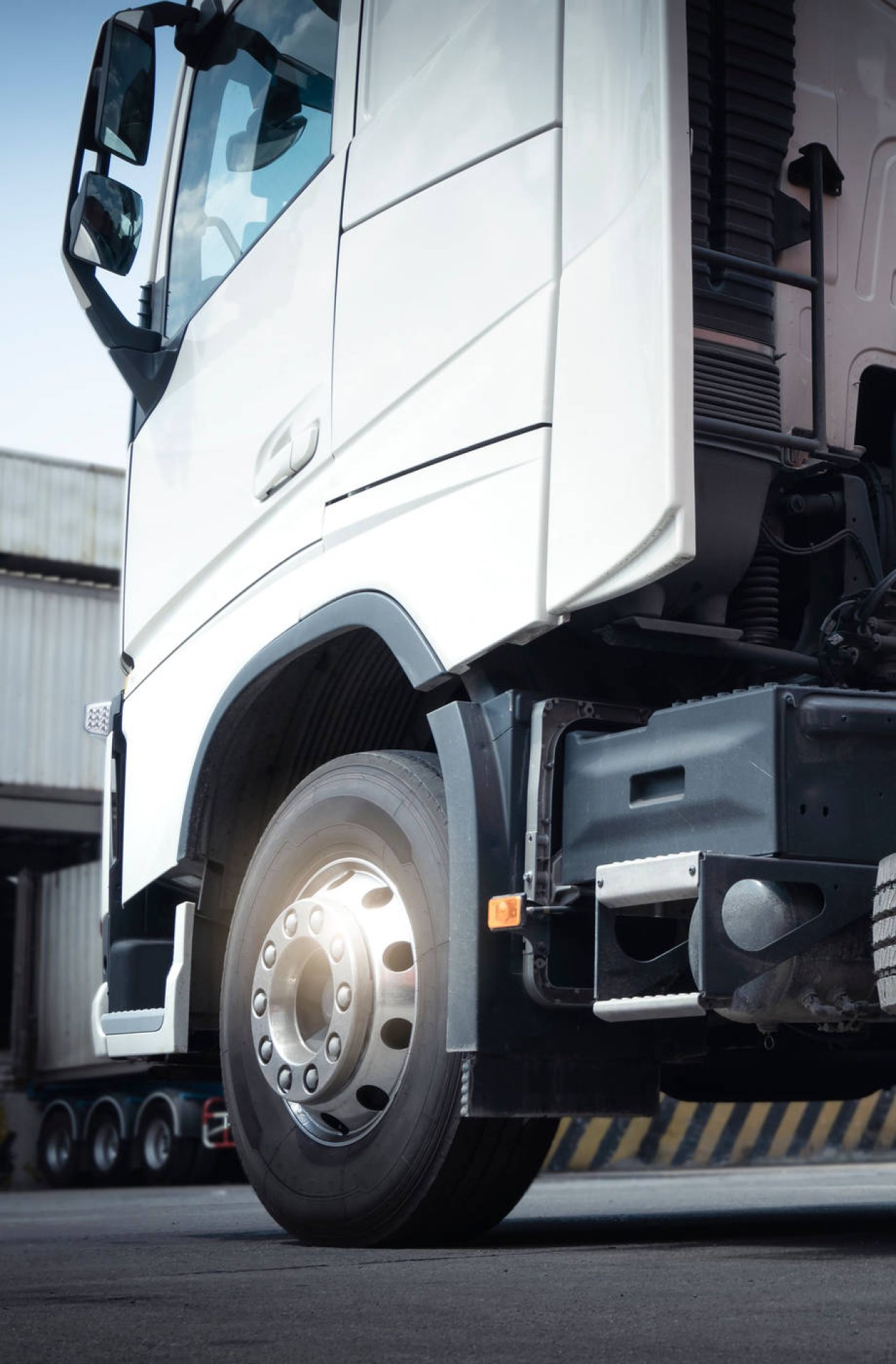 Nahaufnahme eines weißen Lkw-Fahrersitzes und Vorderrads vor einem Industriegebäude.