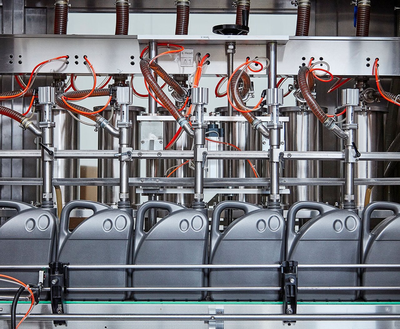 Eine industrielle Abfüllanlage für Flüssigkeiten mit mehreren grauen Kanistern und roten Schläuchen.