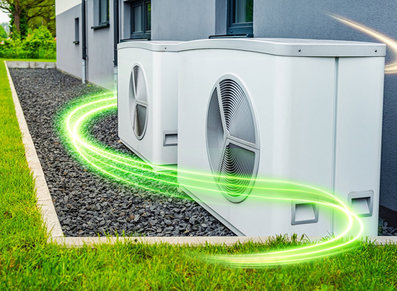 Eine Wärmepumpe im Garten auf einem Kiesbett neben einer Wiese.
